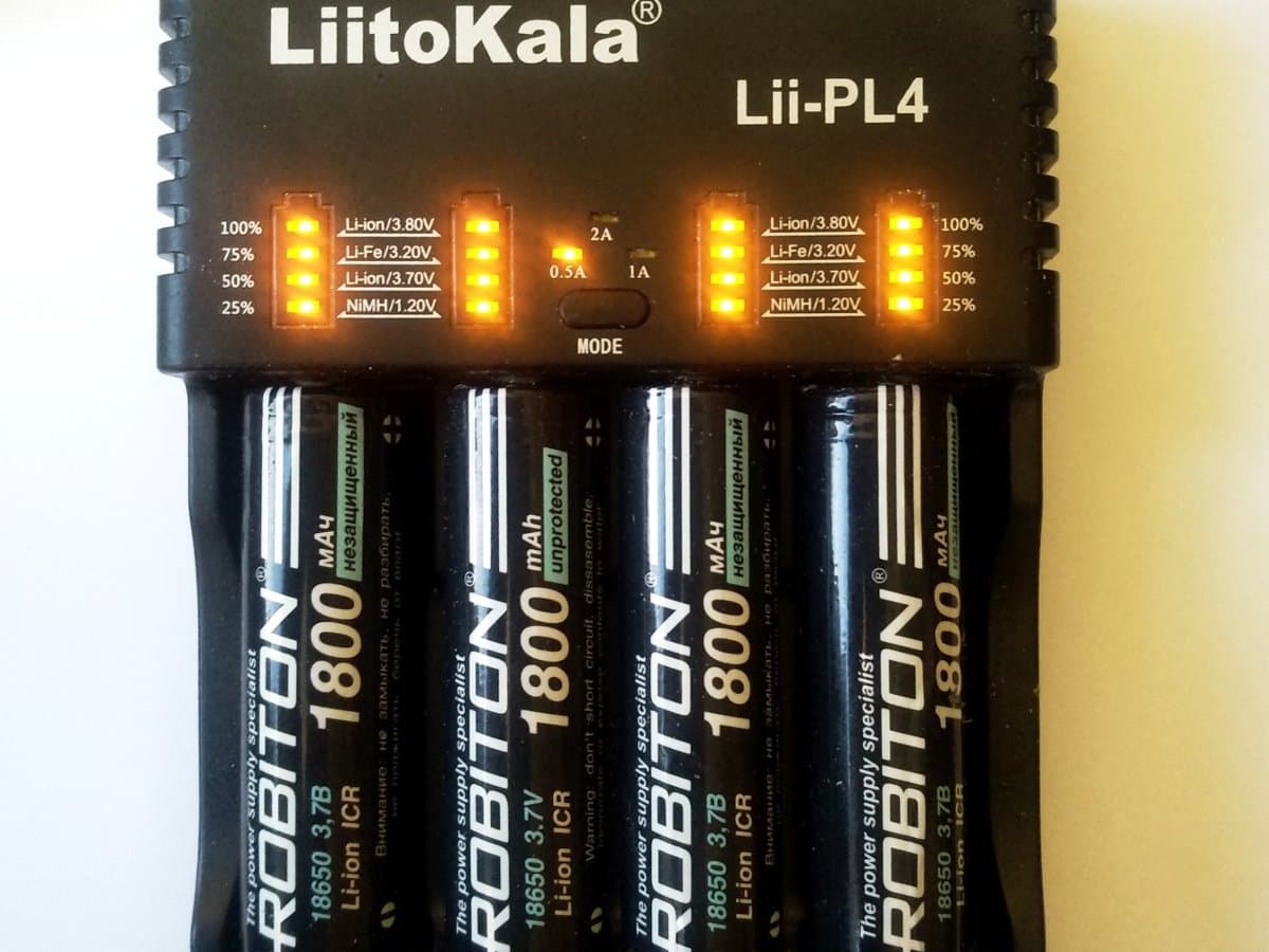 Four black 18650 lithium-ion cells in a four-bay charger with orange charge level lights lit