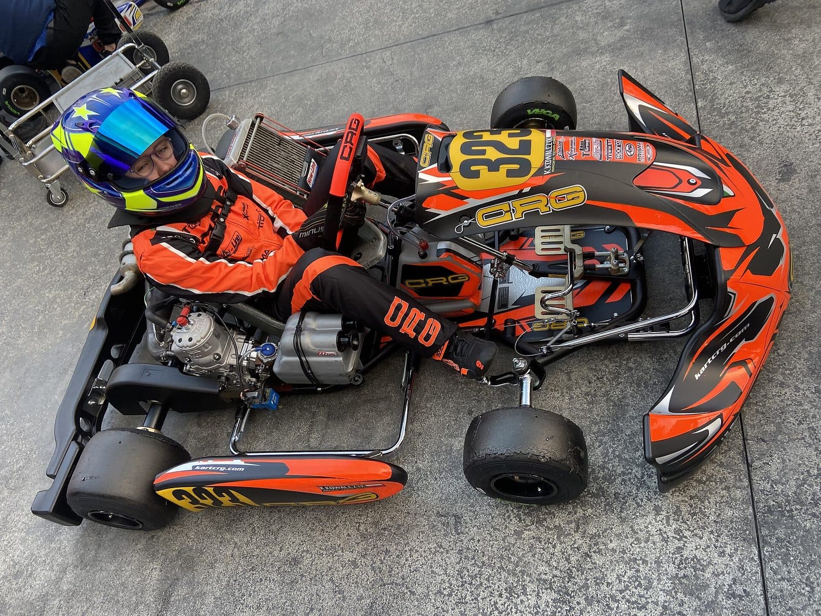 Young kart driver in a helmet and full racing suit sitting in a kart