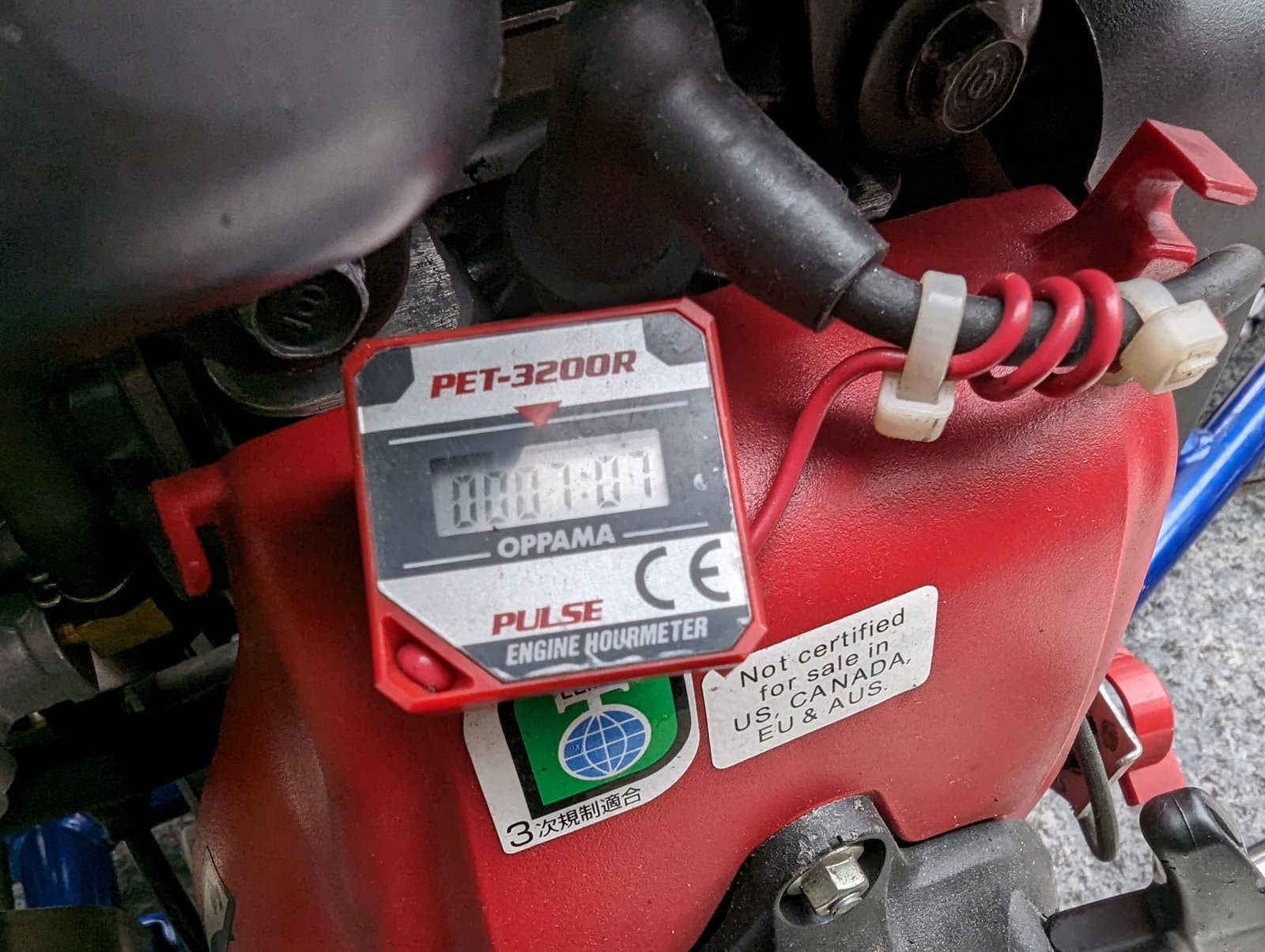 Red engine hour meter on a Honda go-kart engine with a red wire coiled around the black spark plug lead and fixed with two white cable ties