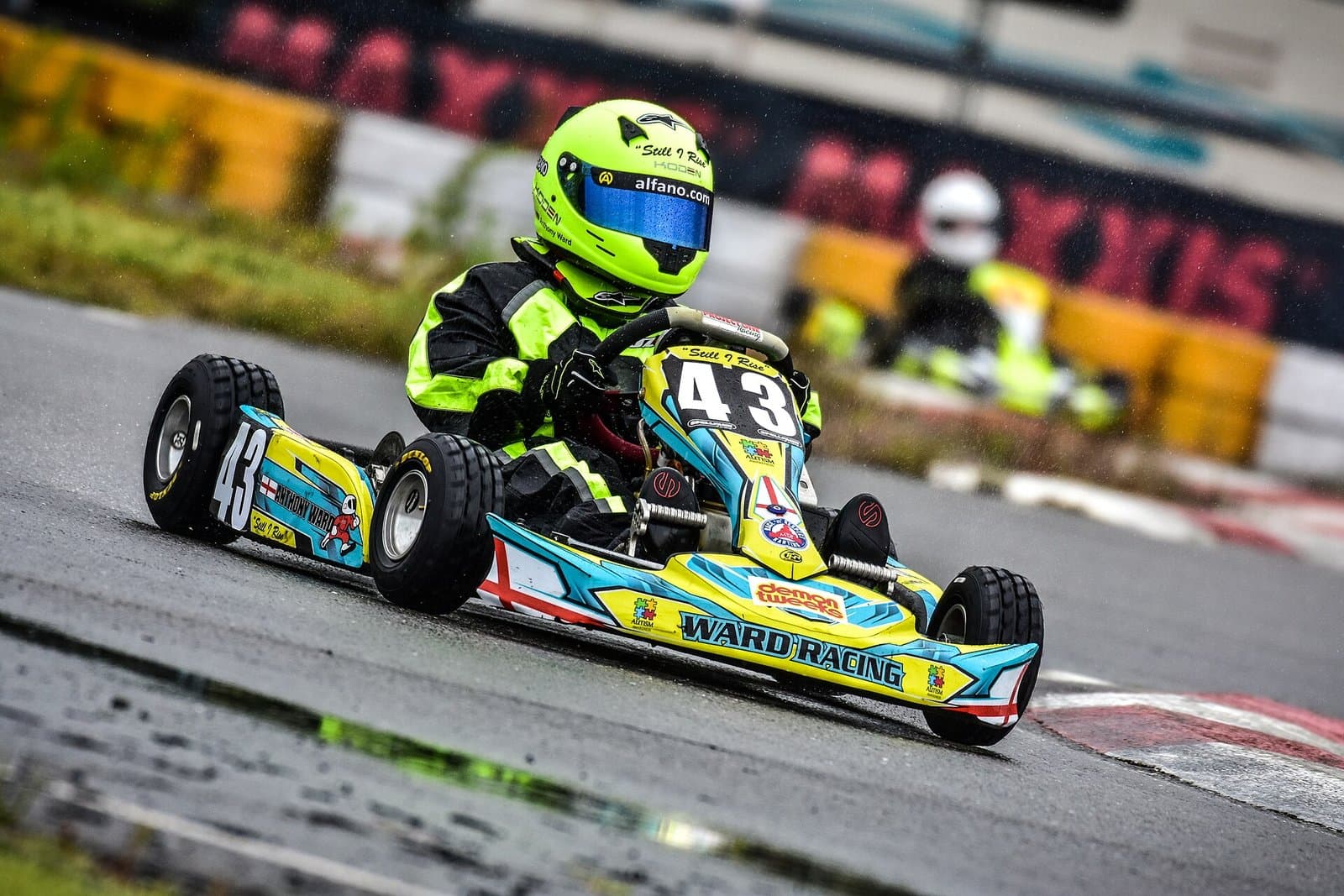 A kart in the rain on wet-weather tires, cornering on a wet track with a driver in a full-face helmet