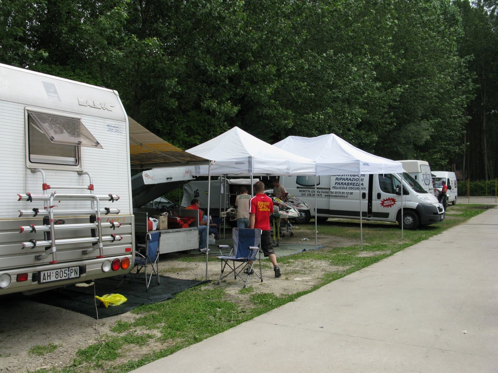 A kart paddock at Pista Winner in Nizza Monferrato, Italy, with white gazebo tents, a motorhome and mechanics working around a kart
