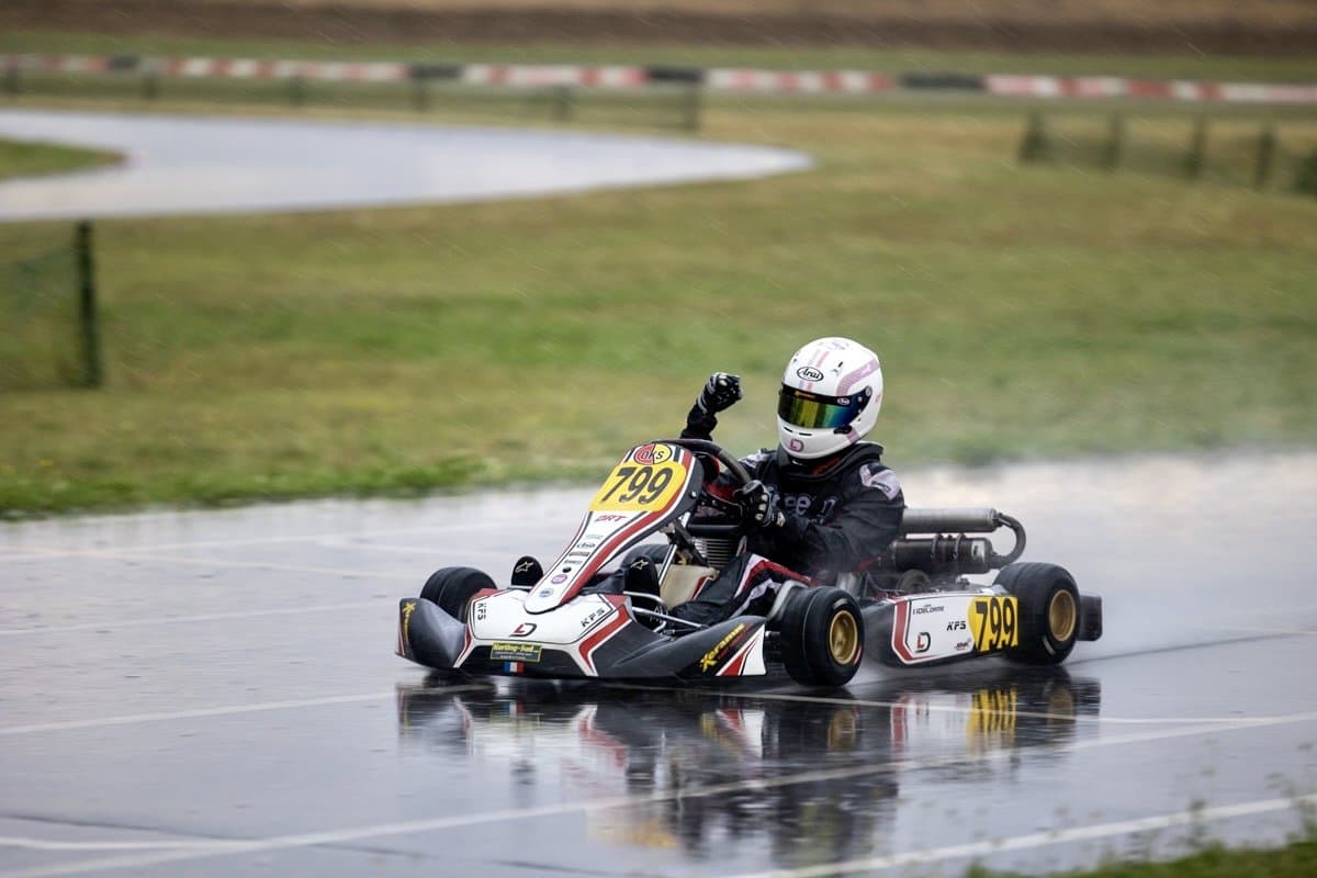 A kart on a soaked circuit in the rain, spray lifting off the rear tyres and the wet tarmac reflecting the kart.