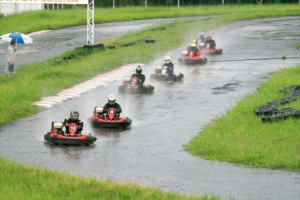 A pack of karts racing through a corner in the rain, spray hanging over the soaked track and hiding the karts behind.